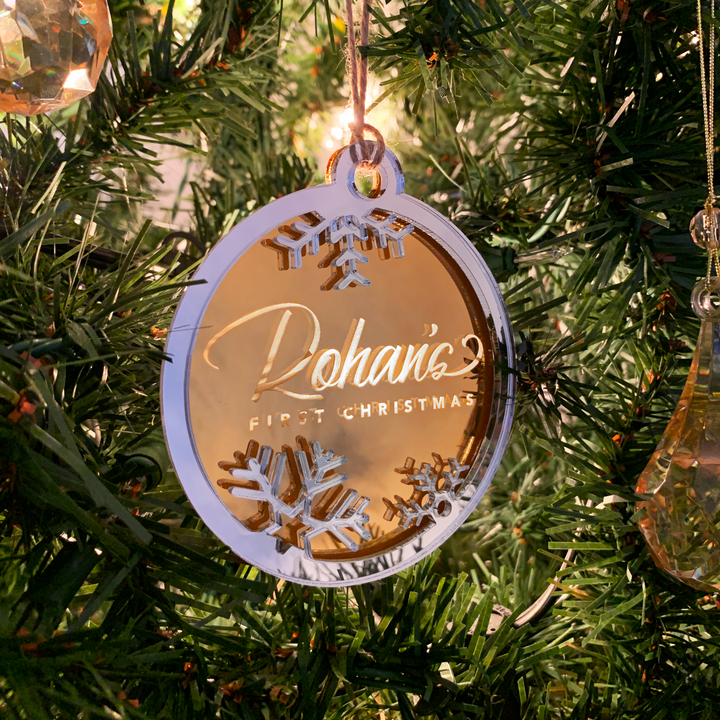 A Christmas tree decorated with ornaments, including a round ornament with the name "Dahlia" and the text "First Christmas" written on it.
