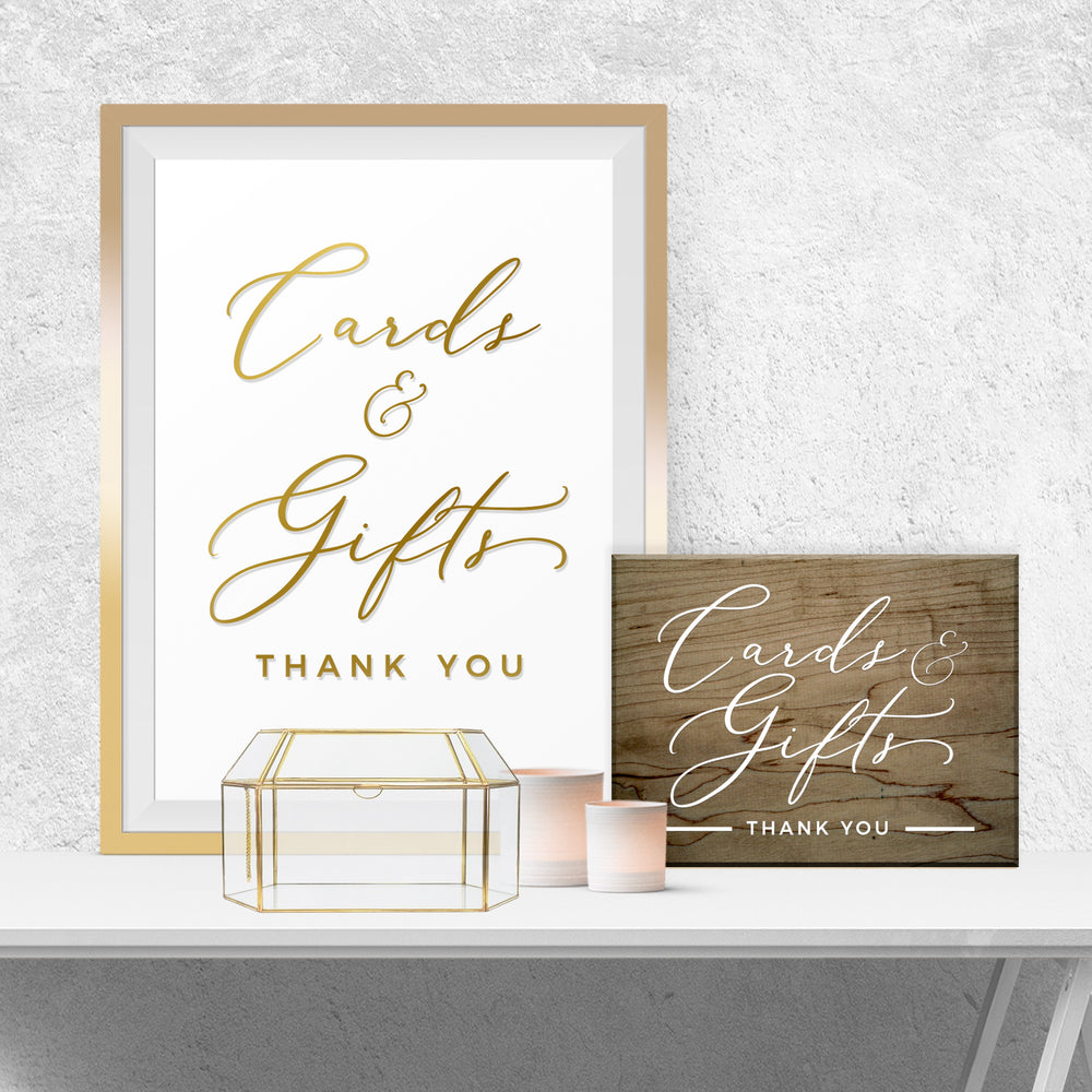 a framed sign that reads "Cards & Gifts Thank You" and a wooden sign that reads "Cards & Gifts Thank You". There is also a small glass box and two candles on a white surface.