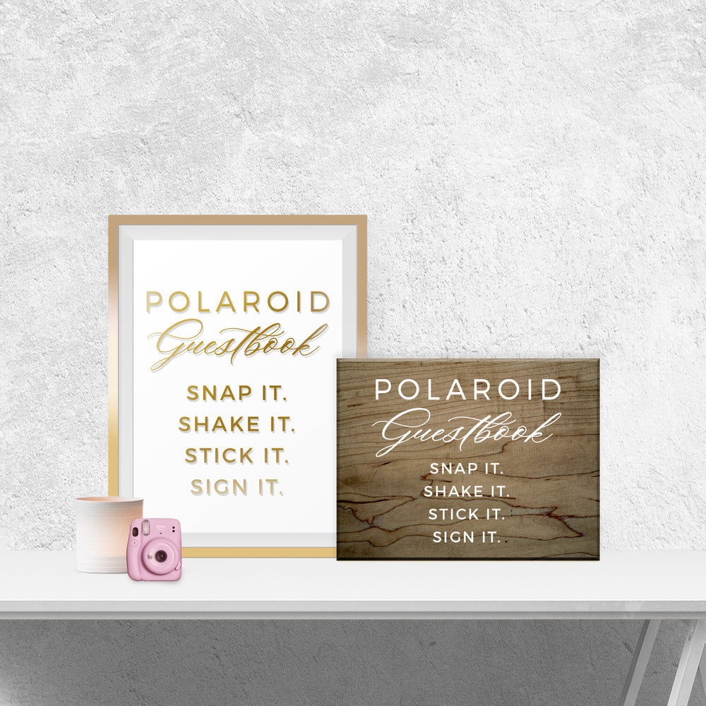 two framed signs on a white shelf, one with a pink camera and the other with a wooden sign.