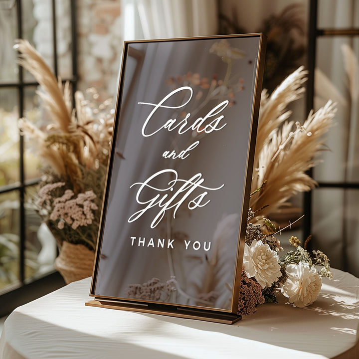A sign displaying "Cards and Gifts" with a "Thank You" message, placed on a table with dried flowers and potted plants.