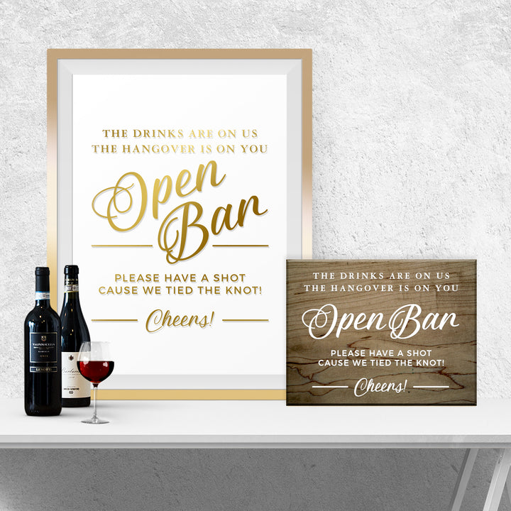 a framed sign with a message about an open bar, accompanied by a wine bottle and a wine glass on a white surface.