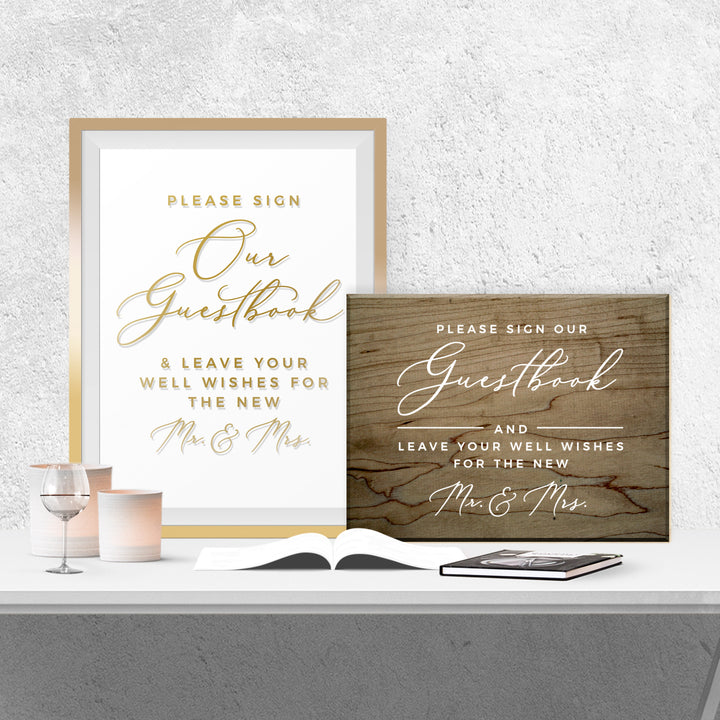 two framed signs on a table, one with a white background and gold lettering, and the other with a wooden background and gold lettering. The signs are titled "Our Guestbook" and "Please Sign Our Guestbook".