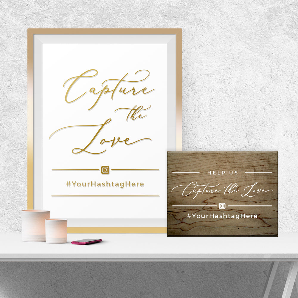 a framed sign with the text "Capture the Love" and a wooden sign with the text "Help us Capture the Love" on a white table. There is also a small object, possibly a candle, and a cell phone on the table.