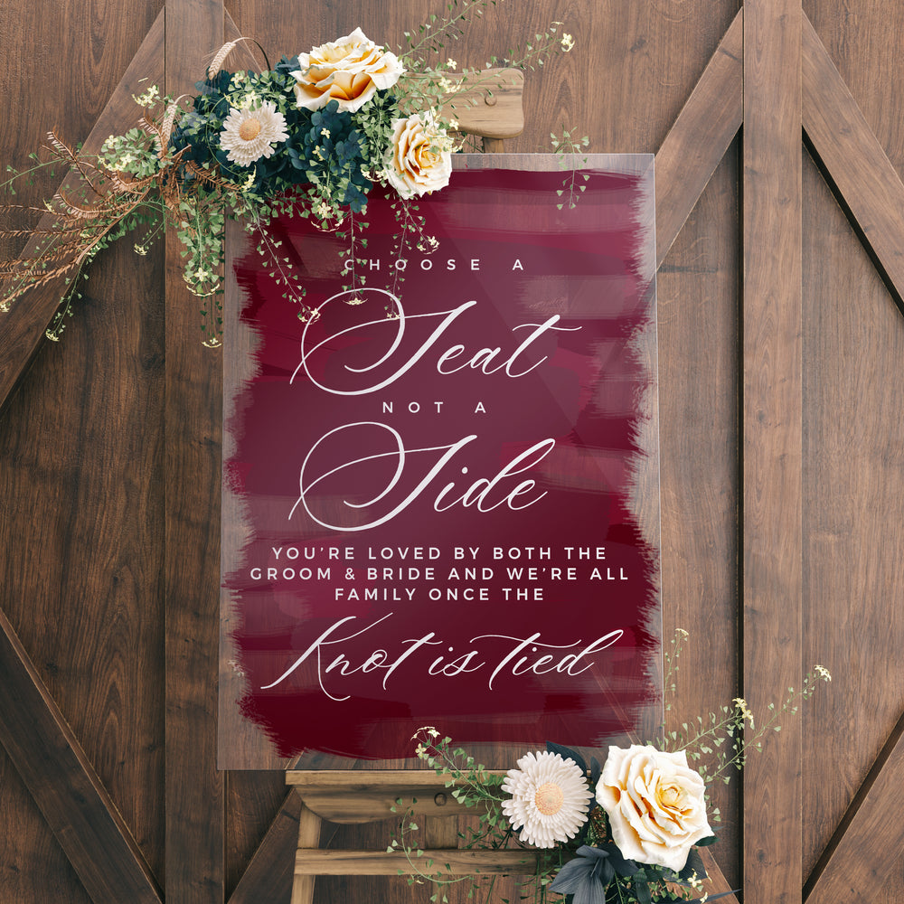 a sign with a maroon background and white text, accompanied by a floral arrangement on a wooden stand.