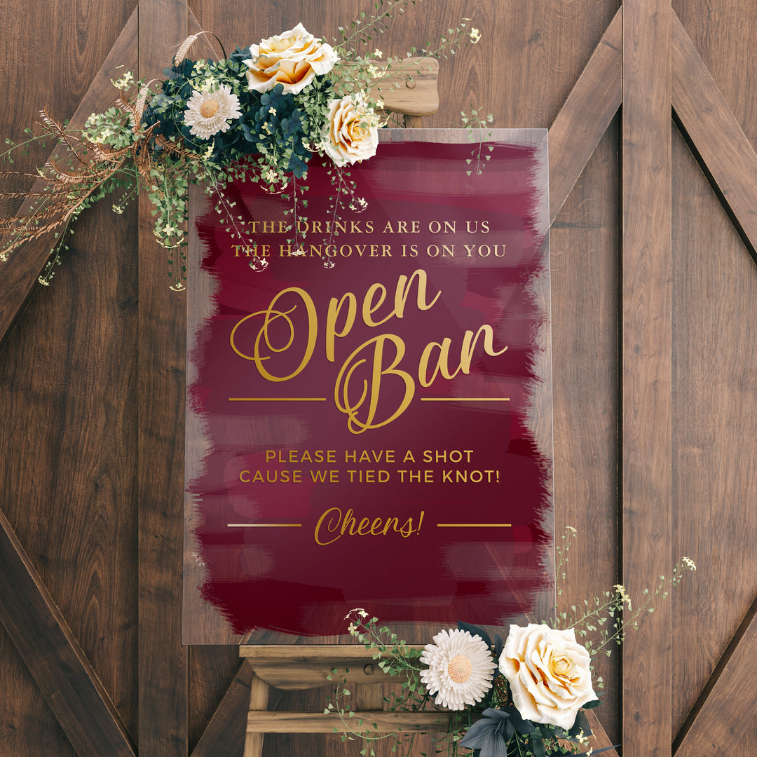 a sign with a maroon background and gold lettering, placed on a wooden easel. The sign reads "Open Ban" and includes a humorous message about the hangover being on the person who drinks.