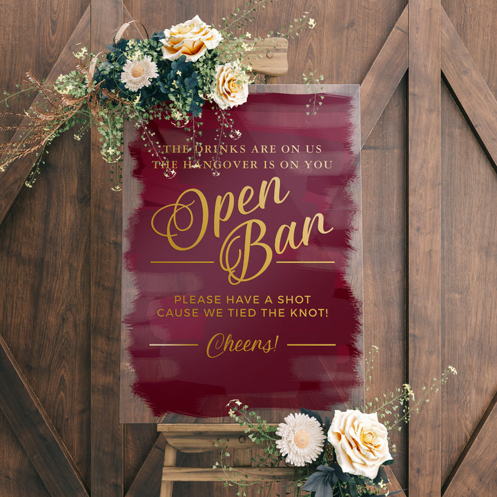 a sign with a maroon background and gold lettering, placed on a wooden easel. The sign reads "Open Ban" and includes a humorous message about the hangover being on the person who drinks.