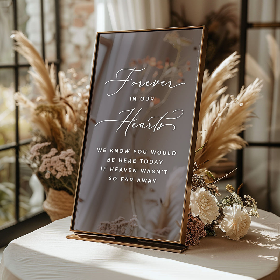 A sign with the message "Forever in our hearts" written on it, placed on a table with flowers in the background.