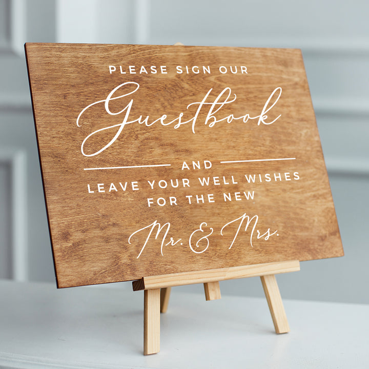 A wooden sign on a stand with a message about guests and well wishes for the new couple.