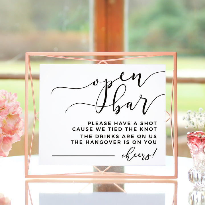 a sign with a message about an open bar, placed on a table with a vase of flowers in the background.