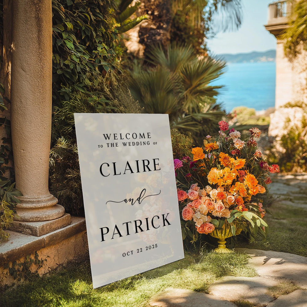 a welcome sign sitting in the grass next to a vase of flowers