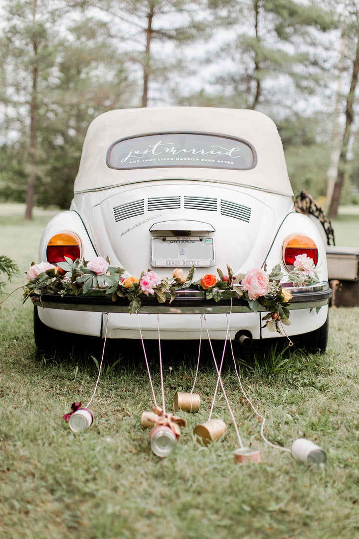 A white wedding car decorated with a floral decal, featuring a bride and groom's names, and various decorative elements such as flowers and a 'Just Married' sign.