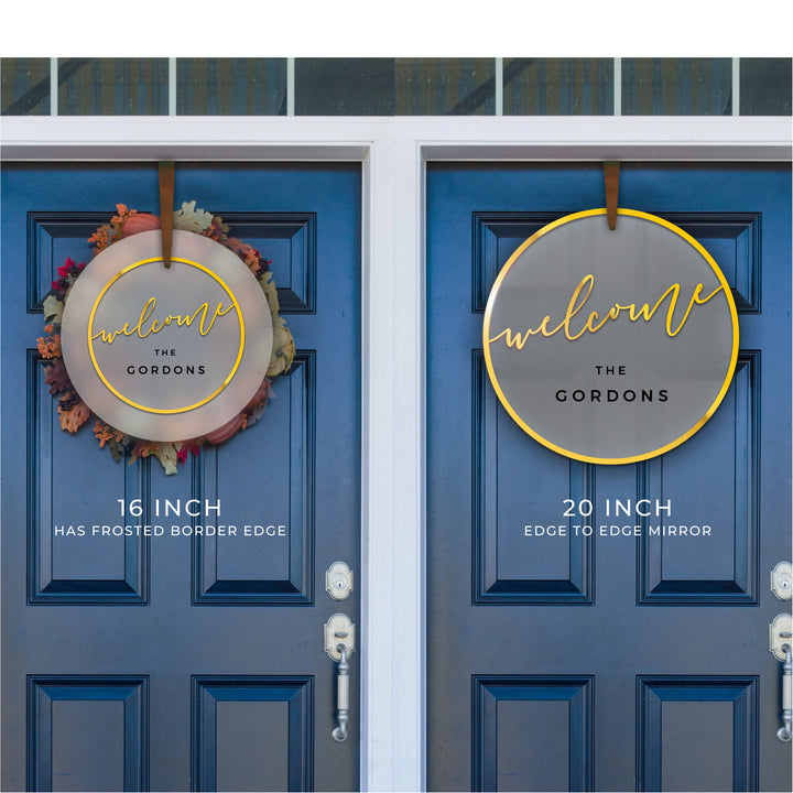 two blue doors with a welcome sign hanging on them. The sign is a circular design with the word "welcome" written in a decorative font. The sign is hanging at a height of 16 inches and has a frosted border edge of 20 inches.