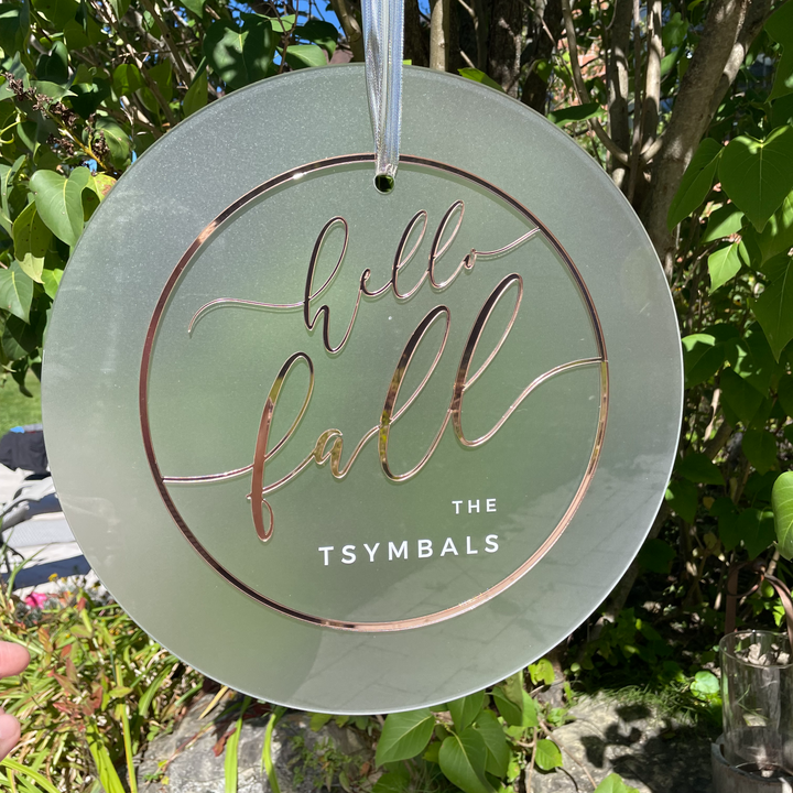 A round sign with the text "Hello fall" on it, surrounded by greenery.