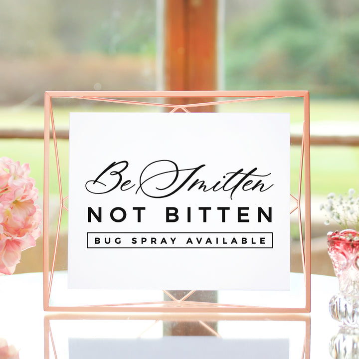 a sign that reads "Be Smitten Not Bitten Bug Spray Available" in a pink frame.