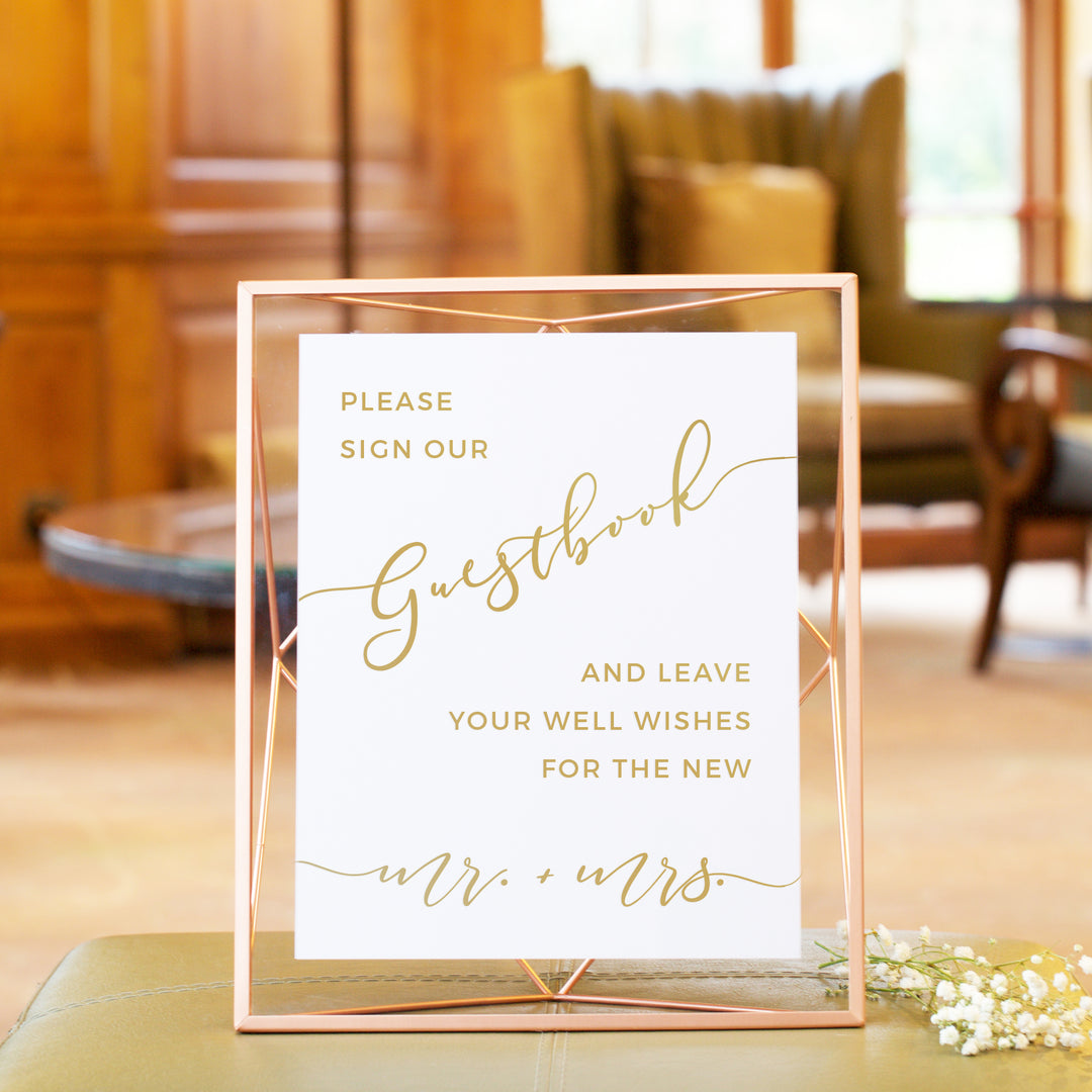 a sign that reads "Please sign our guestbook and leave your well wishes for the new Mr. + Mrs." in a gold cursive font.