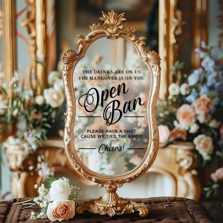 a decorative mirror with a sign in front of it, placed on a table with flowers.