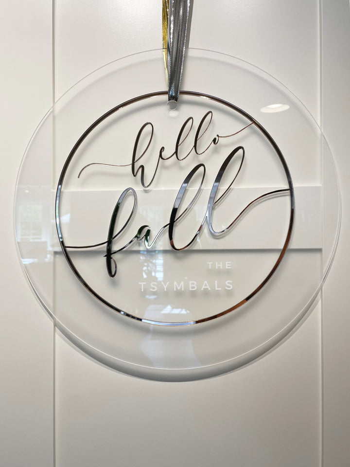 A clear glass sign with the text "Hello fall" written in a cursive font.