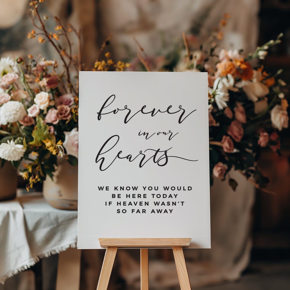 a sign with the message "Forever in our hearts" written on it, placed in front of a floral arrangement.
