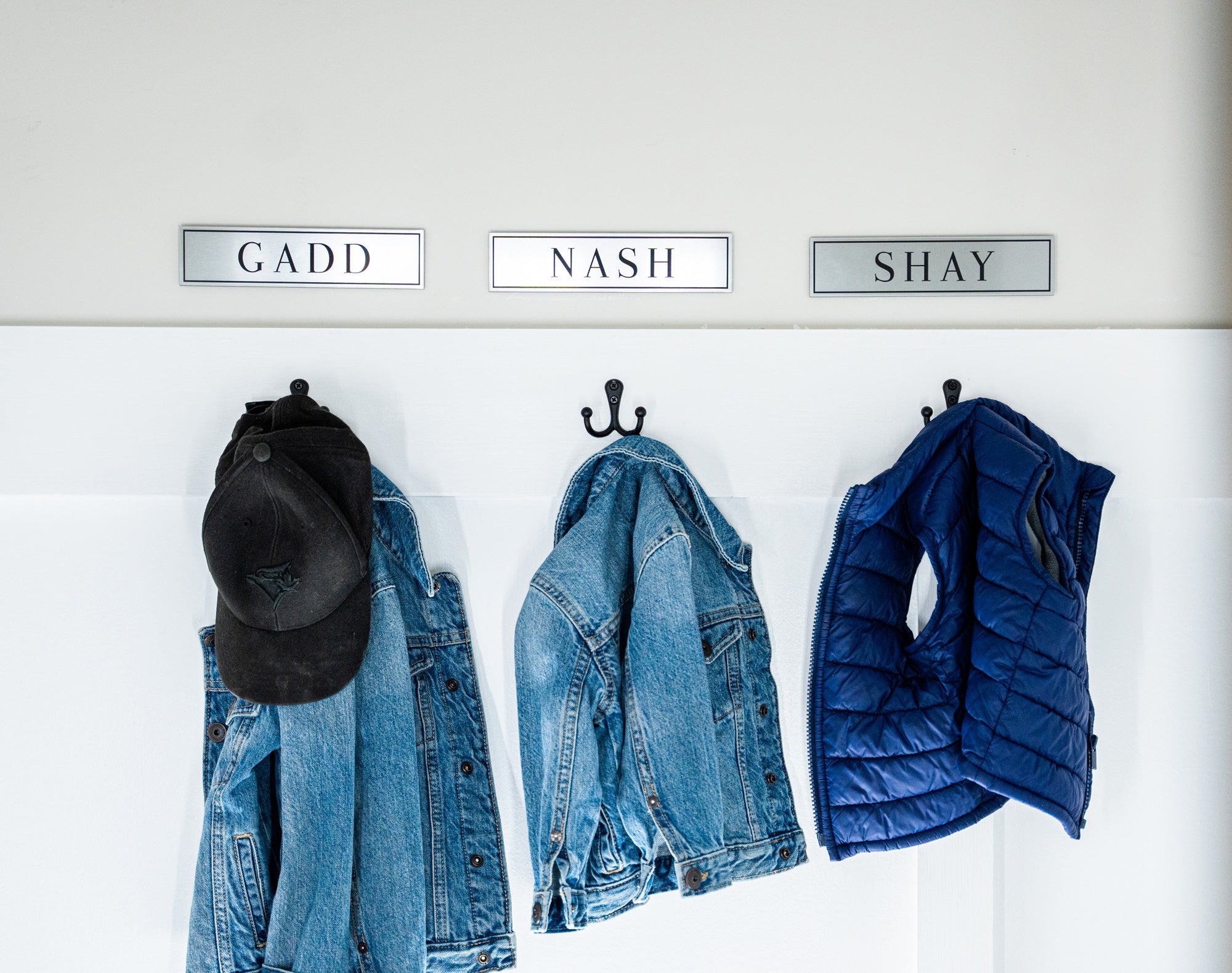 Clothing items including a denim jacket, black cap, and blue puffer vest hanging on hooks with labeled names above.