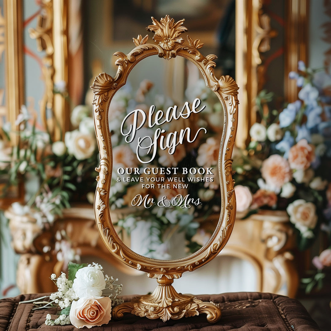 a decorative mirror with a sign in front of it, placed on a table with flowers.