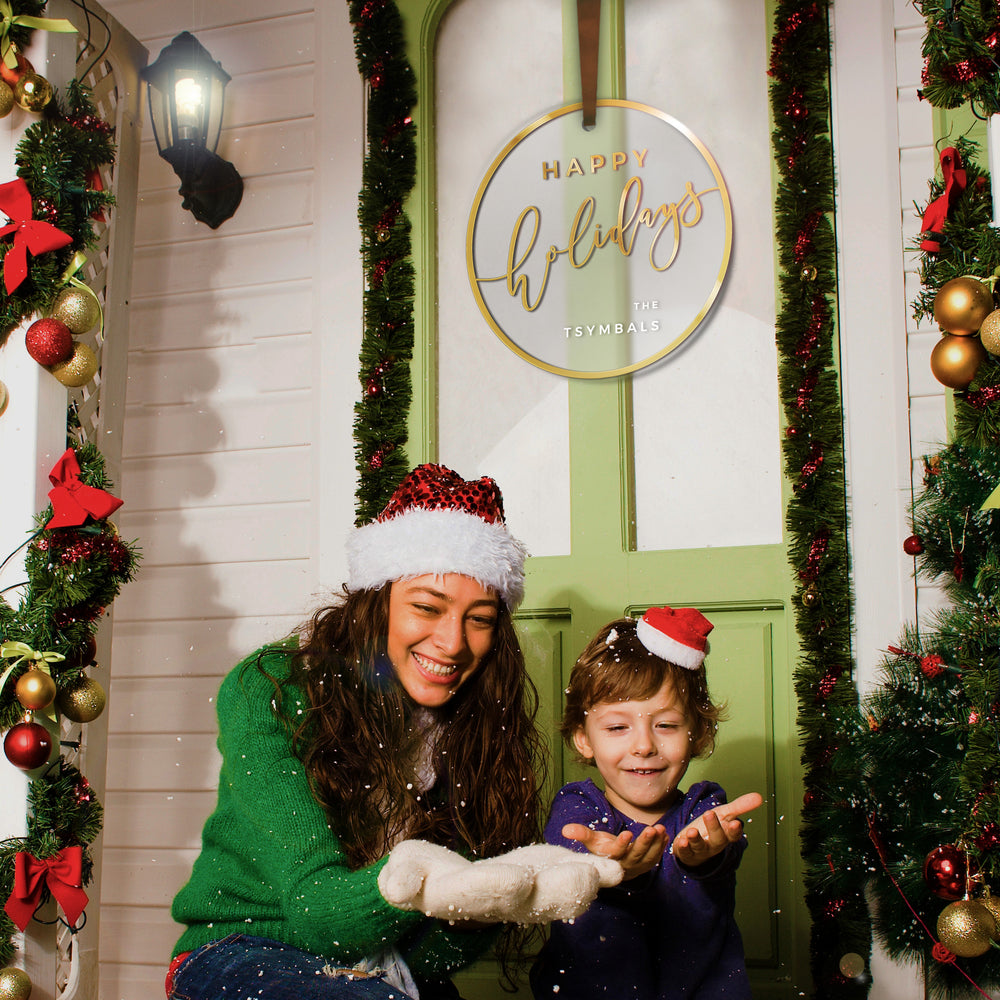 A woman and a child are standing in front of a door decorated with Christmas ornaments, smiling and enjoying the festive atmosphere.
